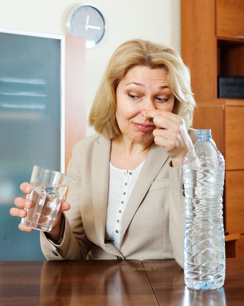 Person holding water glass and bottle, noting water smell like rotten eggs in Phoenix, AZ