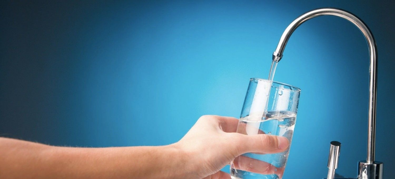 Hand holding glass under running tap water in kitchen sink in Phoenix, AZ