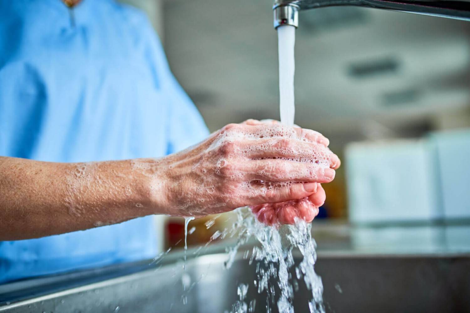 Hands being washed under running tap water with soap in kitchen sink in Phoenix, AZ