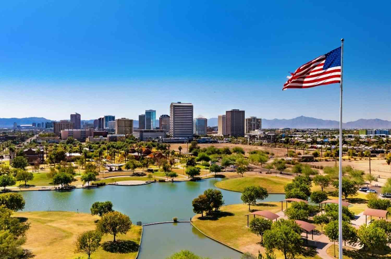 Lakefront park with city skyline and American flag under clear sky in Queen Creek, AZ